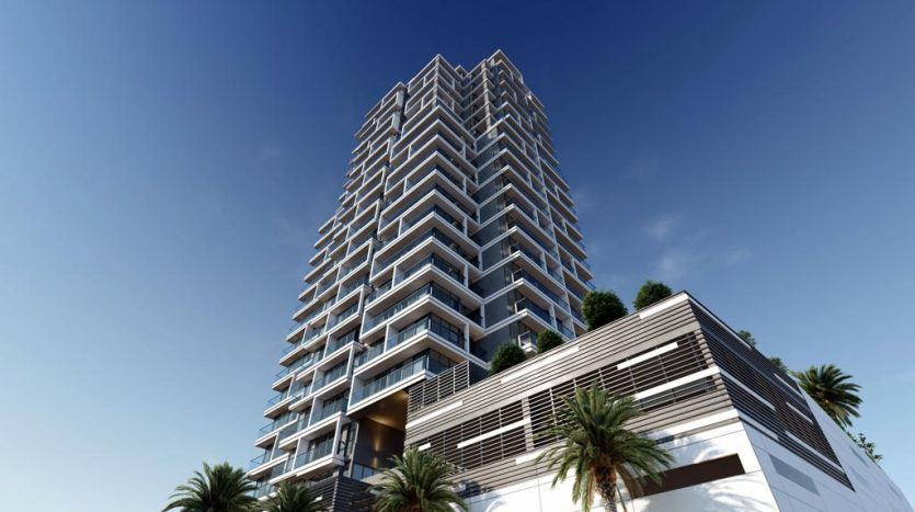 Un immeuble résidentiel moderne de grande hauteur avec des balcons géométriques, situé sous un ciel bleu clair à Dubaï, entouré de palmiers.