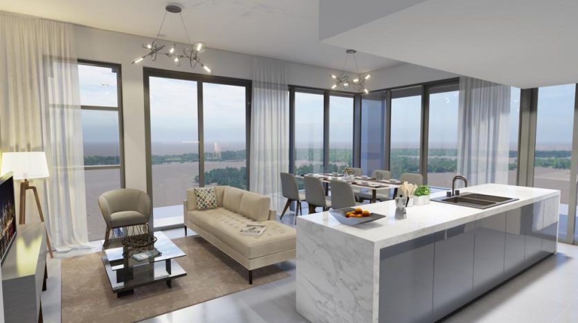 Un intérieur d&#039;appartement moderne et spacieux comprenant une cuisine avec un îlot en marbre blanc, un coin repas, un salon avec de grandes fenêtres laissant passer la lumière naturelle et une vue panoramique sur Catch Dubai à l&#039;extérieur.