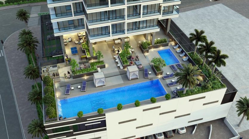 Vue aérienne d'un immeuble d'appartements moderne doté d'une piscine extérieure luxueuse, dotée de chaises longues, de cabanes et entouré d'un aménagement paysager luxuriant conçu pour refléter l'ambiance de Dubaï.
