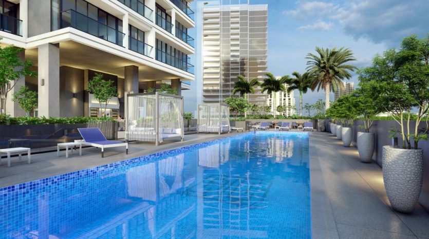 Une luxueuse piscine extérieure dans un hôtel moderne, entourée de chaises longues, de grands bacs à la verdure luxuriante et de bâtiments résidentiels contemporains sous un ciel nuageux, conçue pour capter l'essence de Dubaï.