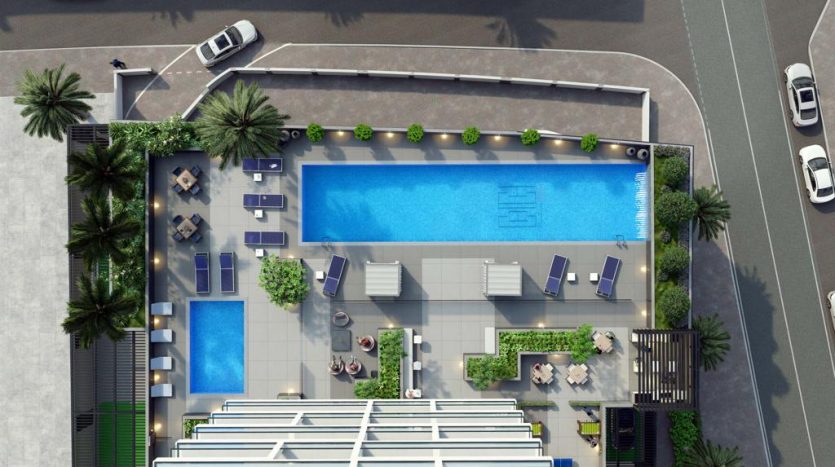Vue aérienne d'une piscine extérieure de luxe avec chaises longues, entourée de palmiers, de petites piscines et d'un parking adjacent. Un design minimaliste avec des formes géométriques domine l'aménagement près de Catch Dubai.