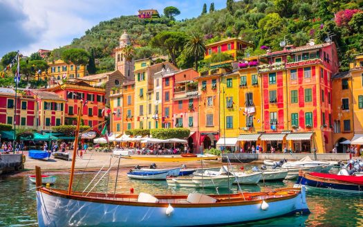 Bâtiments colorés le long d'un front de mer animé dans les collines de Portofino Damac, avec des bateaux amarrés au premier plan sous un ciel lumineux et ensoleillé.