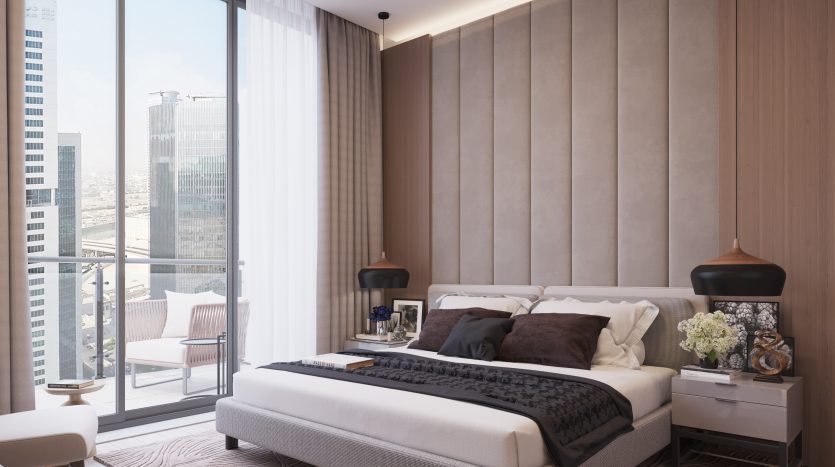 Une chambre moderne dans un appartement de Dubaï comprenant un lit king-size avec une literie blanche et marron foncé, adjacent à des baies vitrées donnant sur un paysage urbain, décoré avec une décoration subtile et des tons terreux.