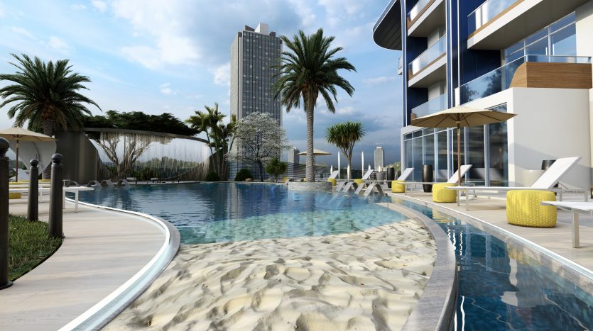 Une piscine luxueuse avec des vagues bleu clair, entourée de bords de plage de sable, de chaises longues sous des parasols et flanquée de bâtiments modernes et de palmiers sous un ciel nuageux à Samana Dubaï.