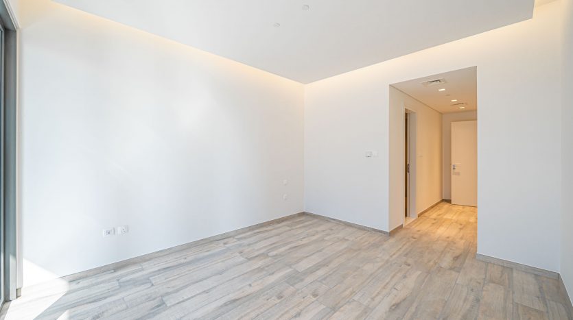 Un appartement vide et bien éclairé à Dubaï avec du parquet, des murs blancs et une porte entrouverte menant à une autre pièce.
