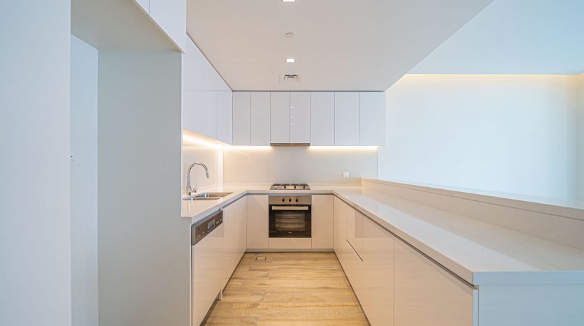 Intérieur de cuisine moderne dans un appartement de Dubaï avec armoires blanches, éclairage à bande LED, appareils intégrés et parquet en bois clair, montrant un design minimaliste et épuré.