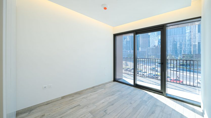 Appartement moderne et vide avec parquet en bois clair, grandes fenêtres offrant une vue sur la ville et murs et plafonds blancs minimalistes, disponible auprès d&#039;une agence immobilière de premier plan à Dubaï.