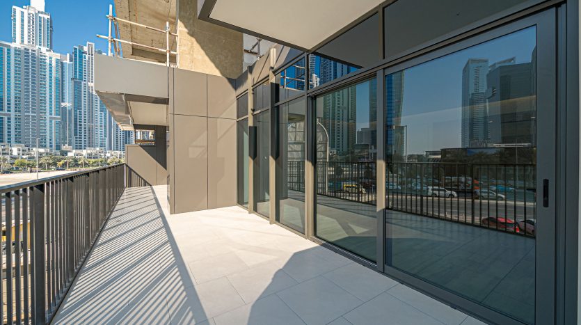 Un balcon urbain moderne avec de grandes portes vitrées offrant une vue sur des immeubles de grande hauteur sous un ciel bleu clair, parfait pour ceux qui cherchent à investir à Dubaï.