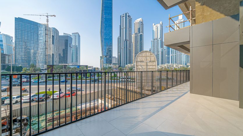 Une vue depuis un balcon en hauteur surplombant un paysage urbain animé avec des gratte-ciel modernes, une route très fréquentée bordée de voitures et un ciel bleu clair au-dessus de Dubaï.