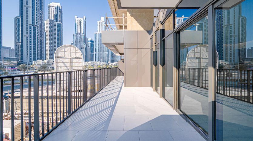 Un balcon spacieux avec des carreaux blancs modernes surplombe un paysage urbain avec d&#039;imposants gratte-ciel sous un ciel bleu clair à Dubaï.