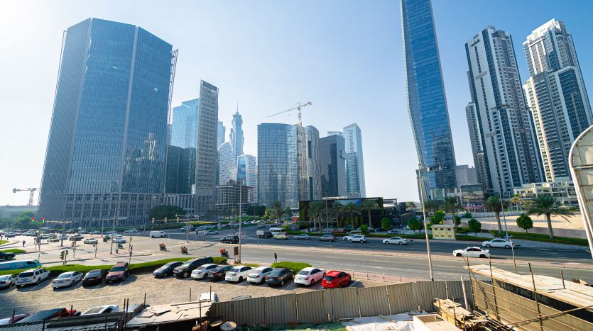 Horizon urbain moderne avec des gratte-ciel en construction à Dubaï, une rue animée remplie de voitures au premier plan et un ciel bleu clair.