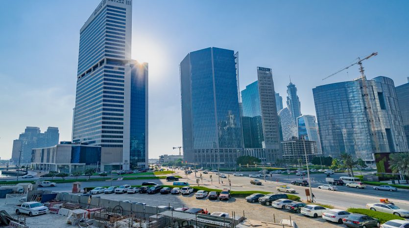Vue grand angle d&#039;un paysage urbain animé avec des gratte-ciel modernes avec le soleil derrière un grand bâtiment, une route très fréquentée, des voitures garées et des constructions immobilières à Dubaï