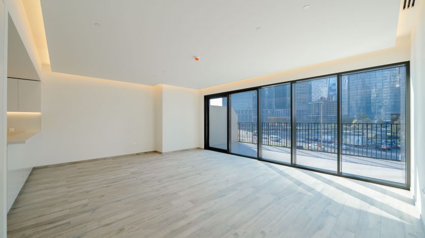 Un appartement vide et moderne à Dubaï avec de grandes fenêtres offrant une vue sur la ville, du parquet, des murs blancs et un éclairage indirect minimaliste au plafond.