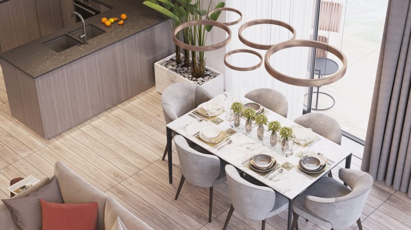 Une cuisine et un coin repas modernes avec une table à manger en marbre pour quatre personnes, entourée de chaises grises moelleuses, adjacente à un îlot de cuisine élégant. Des suspensions circulaires uniques planent au-dessus, offrant une vue imprenable sur la ville
