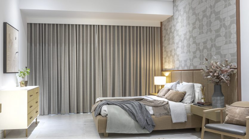 Chambre moderne avec un lit queen-size, un papier peint à motifs géométriques, un grand rideau gris, des meubles en bois dans une villa de Dubaï et une lampe de chevet doucement éclairée.