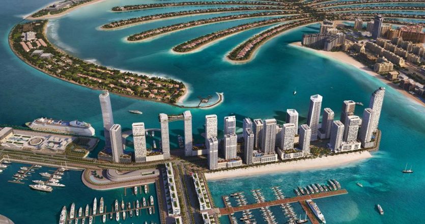 Vue aérienne d&#039;une ville côtière moderne avec des îles artificielles en forme de palmiers, des immeubles de grande hauteur, des marinas et des eaux turquoise claires le long du front de mer.