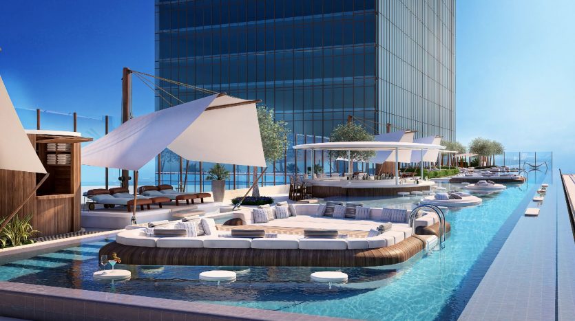 Espace luxueux au bord de la piscine dans un hôtel moderne de Dubaï, doté de sièges luxueux, de cabanes et de parasols avec vue sur l&#039;océan, adjacent à un élégant bâtiment de grande hauteur.