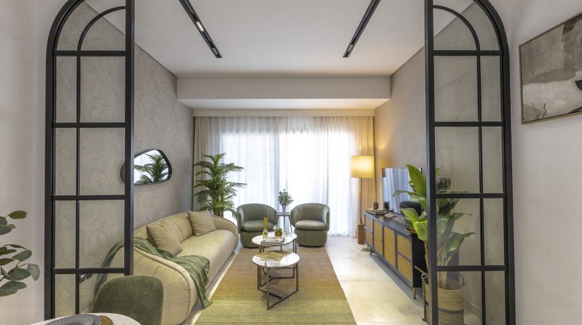 Un salon élégant dans une villa de Dubaï comprenant un canapé en velours vert, une table basse en bois et de grandes fenêtres avec des rideaux transparents. Un éclairage sur rail élégant et des cadres d&#039;arcade avec des plantes ajoutent au décor.