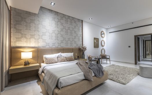 Chambre moderne dans une villa Dubaï avec un grand lit, deux tables de chevet avec lampes, panneaux muraux décoratifs et diverses œuvres d'art. Des couleurs neutres et un tapis à poils longs ajoutent de la chaleur à la pièce spacieuse.
