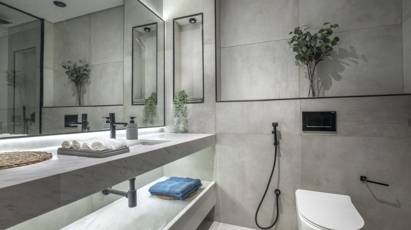Une salle de bain moderne dans une villa à Dubaï, comprenant un grand miroir, un comptoir en marbre blanc avec deux lavabos, des robinets muraux, une douche aux parois de verre et une décoration minimaliste.