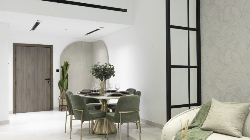 Salle à manger moderne avec table ronde et chaises rembourrées vertes, table élégante, à côté d&#039;un coin salon confortable avec canapé et coussins dans un appartement de Dubaï, aux tons neutres et à la décoration minimaliste