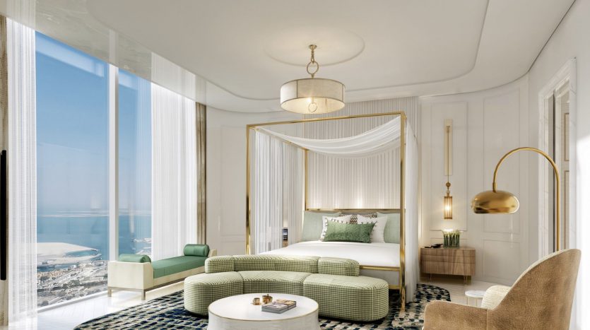 Chambre luxueuse dans une villa à Dubaï, avec un grand lit drapé de blanc, entouré de meubles verts et beiges, un tapis bleu à motifs, des accents dorés et de grandes fenêtres donnant sur la mer.