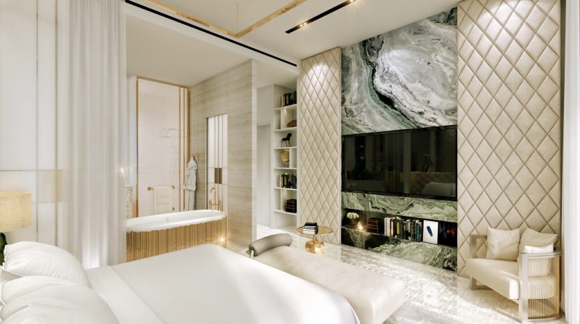 Chambre luxueuse dans une villa de Dubaï avec un lit blanc, des panneaux muraux en marbre dotés d&#039;une cheminée et d&#039;une télévision, du parquet et une salle de bains ouverte connectée visible derrière des portes vitrées.