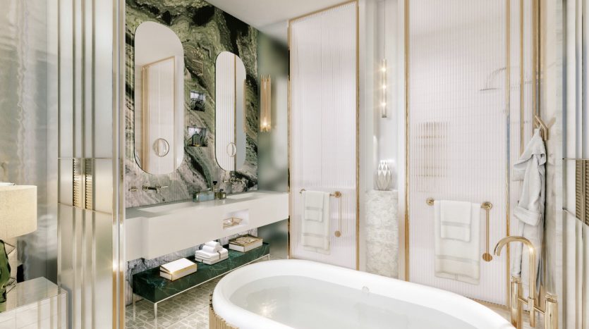 Une salle de bains luxueuse dans un appartement de Dubaï comprenant une grande baignoire ovale, des murs en marbre, des accents dorés, deux miroirs ovales au-dessus d'une double vasque, une cabine de douche en verre, ainsi qu'un éclairage et des serviettes bien placés.