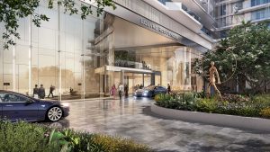 Un rendering artistico dell'ingresso di un moderno hotel chiamato "Louvre Residences" a Dubai, con una facciata in vetro, un'area di parcheggiatori con auto di lusso e persone che camminano in mezzo al verde.