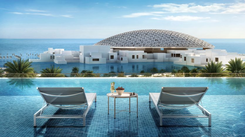 Un rendu architectural d&#039;un bâtiment moderne surmonté d&#039;un dôme à Dubaï au bord de la mer, vu depuis une piscine à débordement ornée de chaises longues et d&#039;une petite table sous un ciel bleu clair.