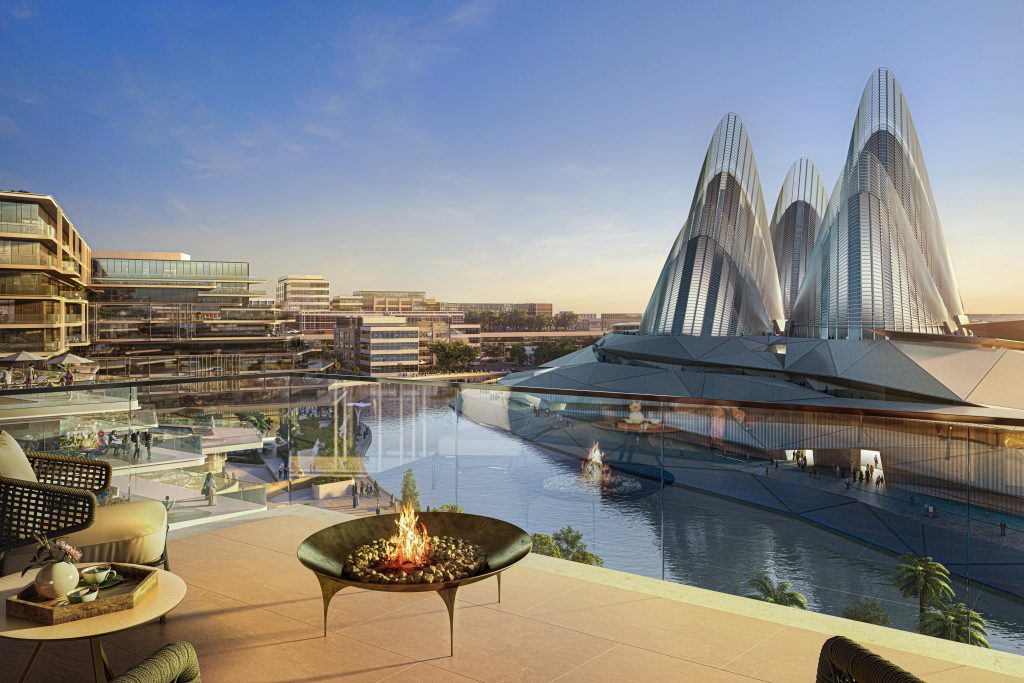 Paysage urbain futuriste au coucher du soleil avec des bâtiments et des tours modernes se reflétant dans un plan d&#039;eau. Le premier plan montre la terrasse d&#039;un luxueux appartement à Dubaï avec un foyer, surplombant la scène.