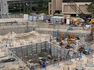 Un cantiere con un'area di scavo piena di vari materiali e attrezzature da costruzione. Al centro del cantiere si vedono degli operai, circondati da muri di cemento e rinforzi in acciaio per una villa a Dubai.