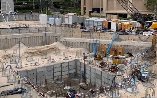 Un chantier de construction avec une zone excavée, remplie de divers matériaux et équipements de construction. Des ouvriers du bâtiment sont visibles au milieu du chantier, entourés de murs en béton et de renforts en acier pour une villa à Dubaï.