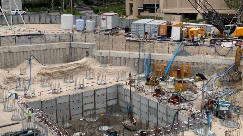 Un chantier de construction avec une zone excavée, remplie de divers matériaux et équipements de construction. Des ouvriers du bâtiment sont visibles au milieu du chantier, entourés de murs en béton et de renforts en acier pour une villa à Dubaï.