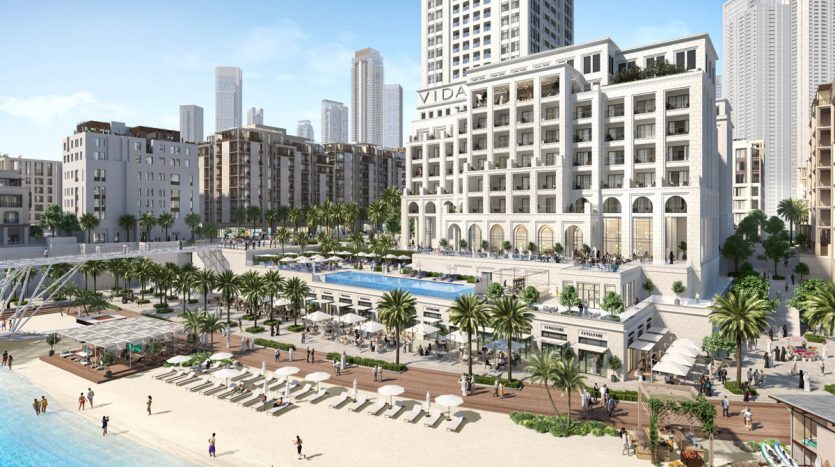 Complexe luxueux en bord de mer avec piscines, chaises longues, palmiers et foule animée, flanqué de grands immeubles modernes sous un ciel dégagé, à proximité du premier immobilier Dubaï.