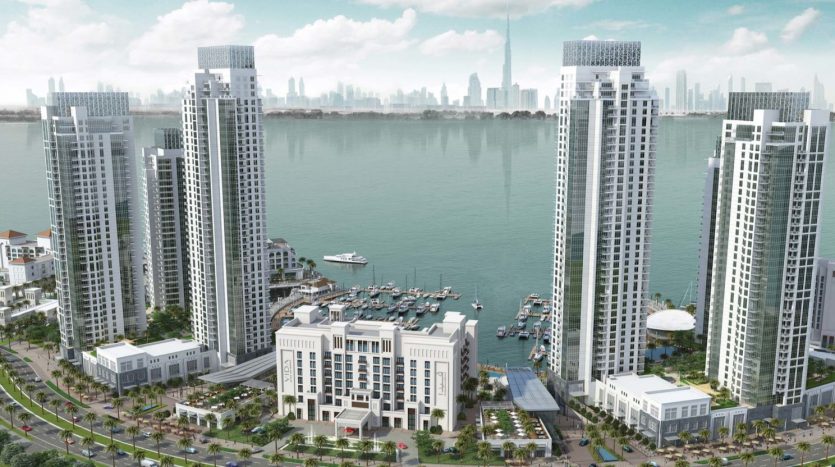 Vue aérienne d&#039;un complexe riverain moderne comprenant de hautes tours résidentielles, des terrains paysagers et une marina avec plusieurs bateaux. Un horizon de la ville est visible en arrière-plan, mettant en valeur les meilleures opportunités d&#039;appartements à Dubaï.