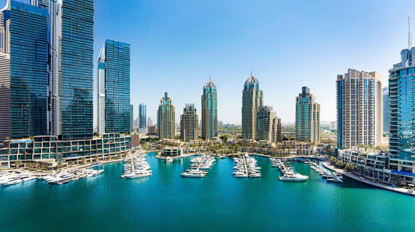 Une vue panoramique sur une marina animée entourée d&#039;immeubles modernes de grande hauteur sous un ciel bleu clair. L&#039;eau est parsemée de nombreux bateaux et yachts, présentant un emplacement idéal pour investir dans le quartier de Dubaï.