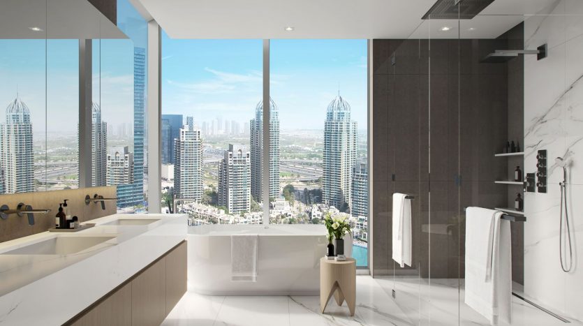 Une salle de bains luxueuse avec de grandes fenêtres offrant une vue sur les toits de la ville, comprenant une baignoire, une douche à l&#039;italienne et deux vasques sur un comptoir en marbre. Idéal pour investir à Dubaï.