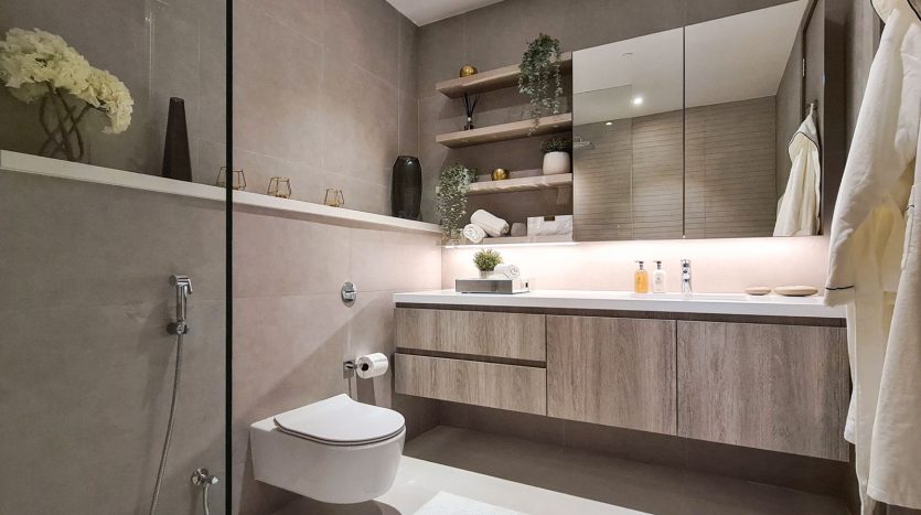Une salle de bain moderne aux tons neutres, comprenant une vasque flottante, des toilettes suspendues, une cabine de douche en verre et des étagères en bois avec des objets décoratifs, idéale pour ceux qui cherchent à investir à Dubaï.