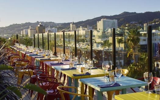 Terrasse extérieure du restaurant dotée de tables et de chaises colorées, surplombant un paysage urbain panoramique de Dubaï avec des collines en arrière-plan sous un ciel clair.