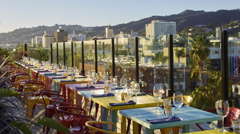Terrasse extérieure du restaurant dotée de tables et de chaises colorées, surplombant un paysage urbain panoramique de Dubaï avec des collines en arrière-plan sous un ciel clair.