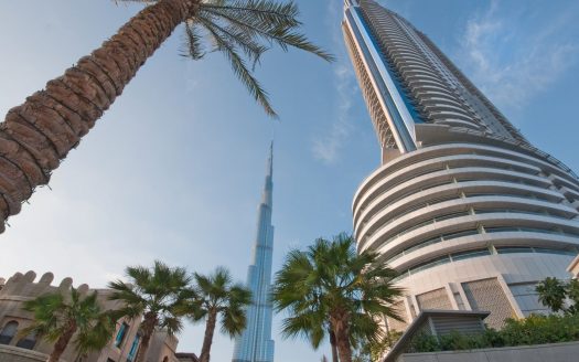 Vue sur le Burj Khalifa et un autre immeuble de grande hauteur entre des palmiers sous un ciel bleu clair, mettant en valeur le premier immobilier de Dubaï.