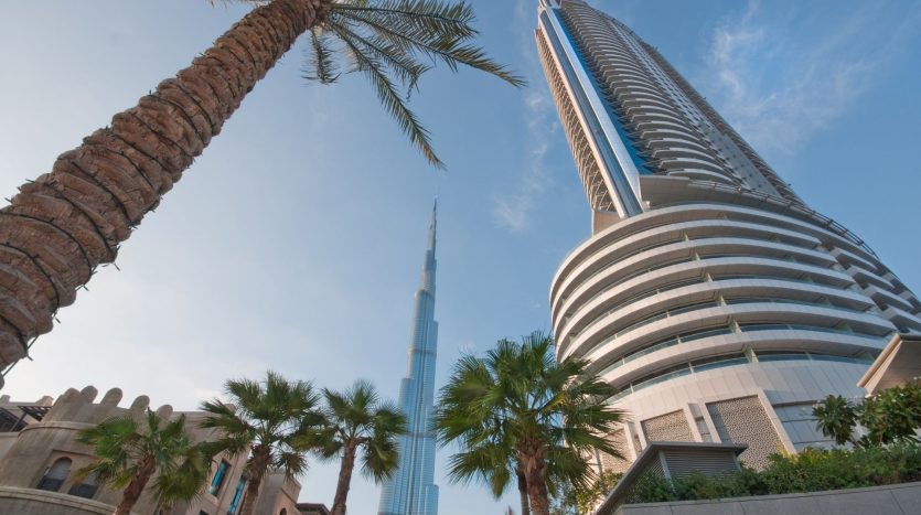 Vue sur le Burj Khalifa et un autre immeuble de grande hauteur entre des palmiers sous un ciel bleu clair, mettant en valeur le premier immobilier de Dubaï.