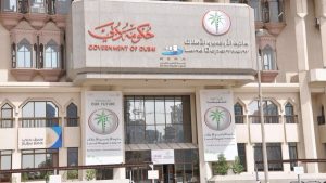 Facciata di un edificio governativo a Dubai, con insegne del Dipartimento del Territorio di Dubai e del RERA, con un'insegna di Dubai Real Estate in basso. L'architettura è moderna con elementi tradizionali.