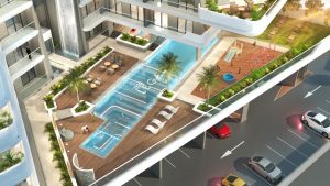 Vue aérienne d'un complexe d'appartements moderne à Dubaï doté d'équipements comprenant une grande piscine, des chaises longues, un terrain de basket-ball et un parking adjacent avec des voitures.