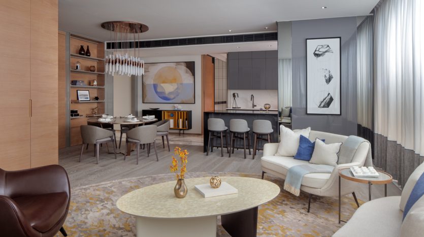 Salon moderne et cuisine ouverte dans un appartement de Dubaï au décor élégant, comprenant un coin salon confortable, un espace salle à manger et des accents muraux artistiques. Les tons neutres avec des touches de bleu créent une atmosphère sereine.
