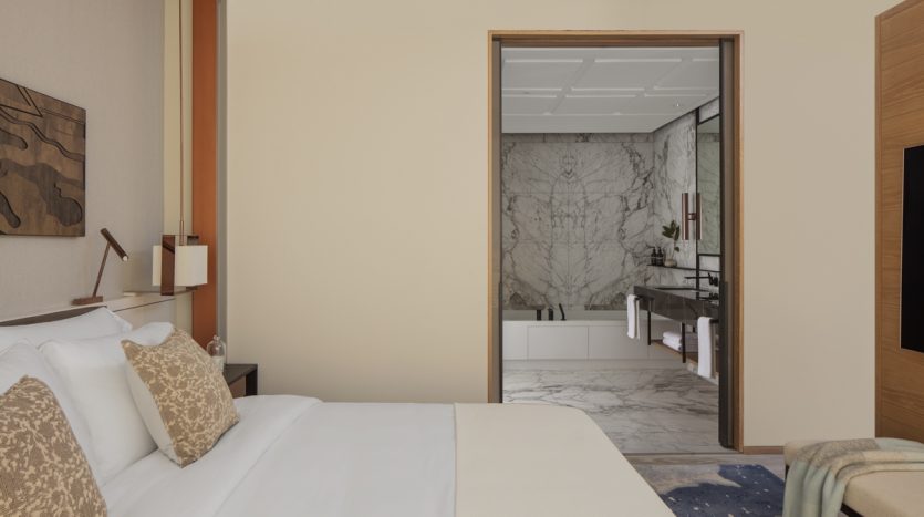 Une chambre moderne dotée d&#039;un lit moelleux avec des oreillers décoratifs et une vue sur une luxueuse salle de bains en marbre attenante. Les tons chauds et neutres et la décoration contemporaine d&#039;un appartement Dubaï renforcent l&#039;atmosphère élégante.
