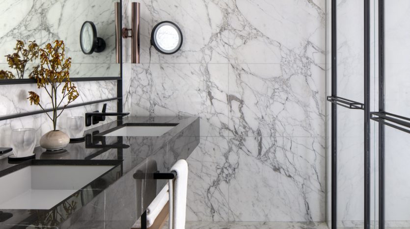 Une salle de bains luxueuse avec de vastes murs et sols en marbre blanc, une élégante vanité noire avec un lavabo rectangulaire, un miroir mural et une cabine de douche en verre. Ce cadre opulent est idéal pour ceux qui sont intéressés