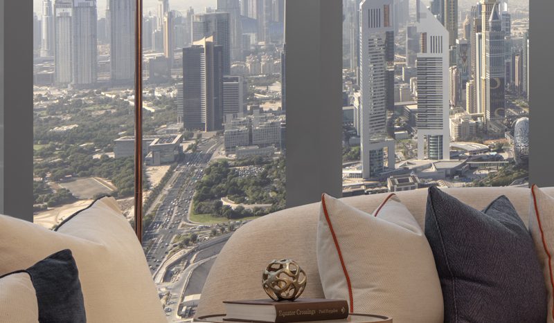 Vue depuis le salon d&#039;un appartement de grande hauteur donnant sur les toits de la ville avec des gratte-ciels modernes et des routes de Dubaï, avec des canapés confortables et une décoration tendance au premier plan.