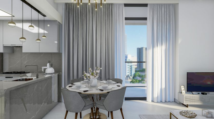 Cuisine moderne avec comptoirs en marbre, coin repas adjacent avec une table ronde pour quatre personnes, donnant sur le paysage urbain de Dubaï à travers de grandes fenêtres et un écran de télévision flou.